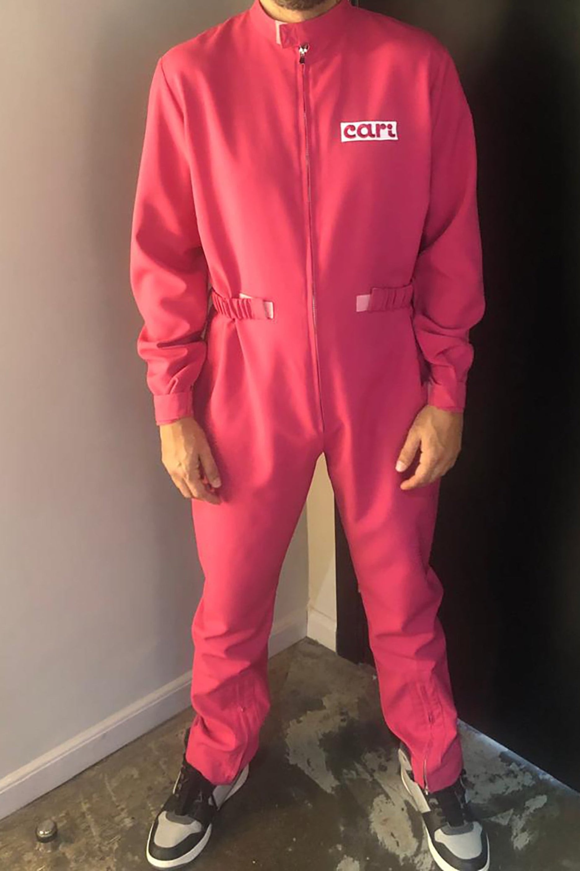 Man wearing a bright pink jumpsuit with a logo, standing indoors.
